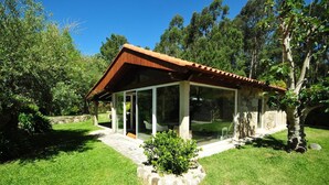 A modern house with a glass extension, surrounded by a well-maintained lawn and trees. - Casa da Luz Charming Cottage w/ Beautiful Garden (Vila Nova de Cerveira)