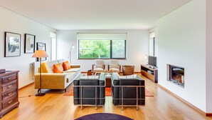 Ein modernes Wohnzimmer mit einer Couch, zwei schwarzen Hocker, einem Couchtisch, einer Lampe, einem Fernseher und einem Kamin.