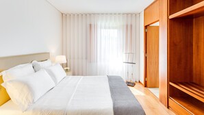 Ein Hotelzimmer mit einem Bett, einem Nachttisch mit Lampe, einem Kleiderschrank und einem Fenster mit leichtem Vorhang.