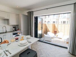 A modern kitchen with white cabinets, a dining area with a table set for breakfast, and a sliding glass door leading to an outdoor seating area.