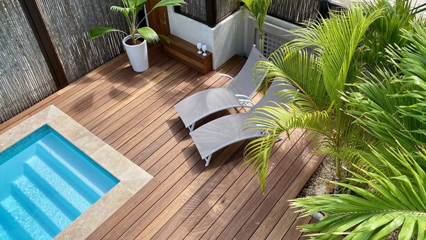 Un terrazzo in legno con piscina, sedie a sdraio e piante in vaso.