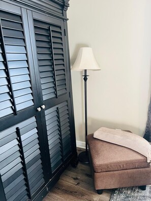 A room with a dark wooden wardrobe, a floor lamp, and a brown sofa.