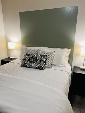 A neatly made bed with a white duvet and patterned pillows, flanked by two bedside tables with lamps.