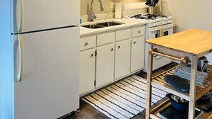 Kompakti keittiö, jossa on valkoiset kaapit, jääkaappi, mikroaaltouuni, liesi ja pesuallas.