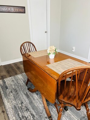 A dining table with four wooden chairs, a woven placemat, and a vase with flowers.