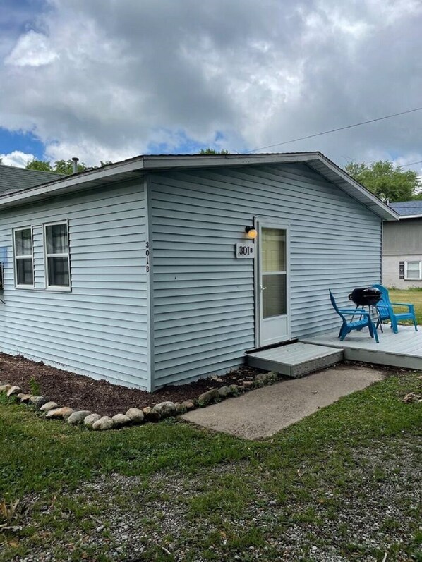 A single-story house with a number '301' on the door, a porch with blue chairs, and a gravel driveway.