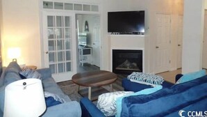 A living room with a sofa, a coffee table, a fireplace, a television, and a ceiling fan. - 2 BR Dog-Friendly Condo W/ Free Golf Cart, Pool and Other Resort Amenities (Myrtle Beach)