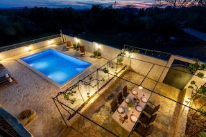 Uma área de piscina no terraço, com piso de pedra, piscina e espaço de refeições com cadeiras e mesas.
