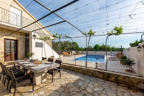Une terrasse en pierre avec une piscine, du mobilier d’extérieur et une table dressée pour les repas.