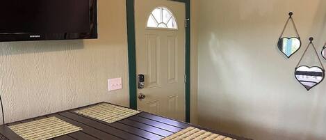 A room with a dark wooden table, a flat-screen TV mounted above it, a door with a green frame, and heart-shaped wall decorations.