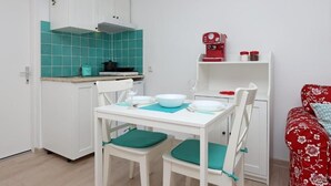 Una cocina pequeña con armarios blancos, salpicadero verde aguamarina y una cafetera roja.
