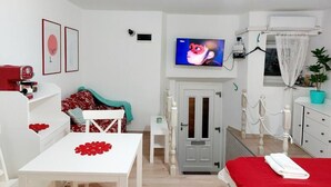 Una habitación con una cama, una mesa cubierta con un mantel rojo, un televisor en la pared y una puerta con picaporte.