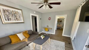 Un salon avec un canapé gris, des fauteuils jaunes, une table basse et un ventilateur de plafond.