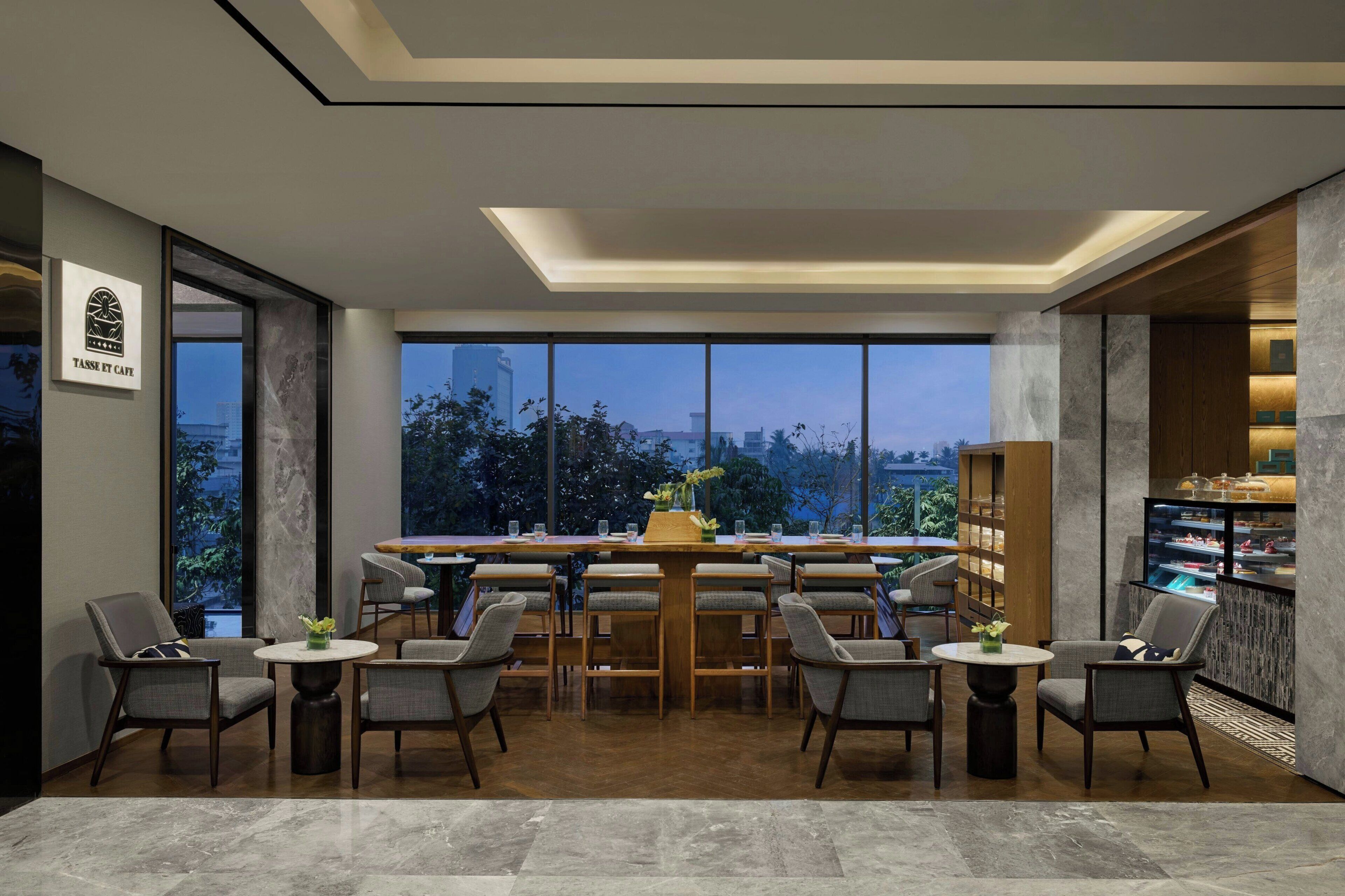 A modern dining area with a large table and chairs, a view of the cityscape, and a dessert display.