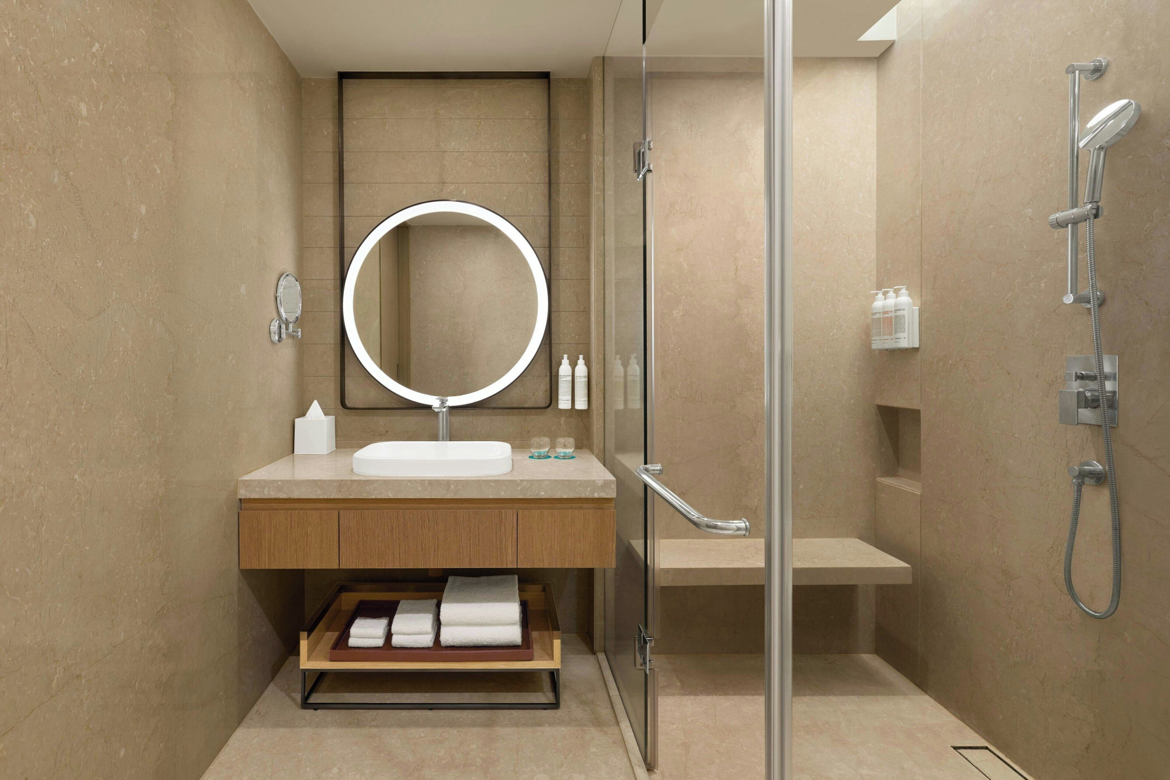 Un baño moderno con cabina de ducha de vidrio, un espejo redondo, un lavabo y un perchero para toallas.