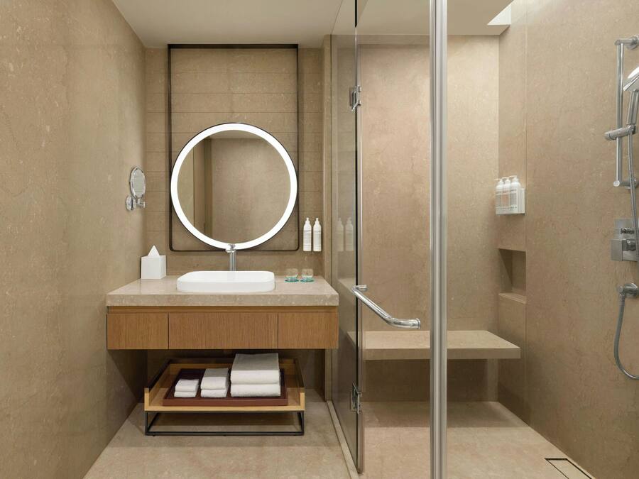 Un baño moderno con cabina de ducha de vidrio, un espejo redondo, un lavabo y un perchero para toallas.