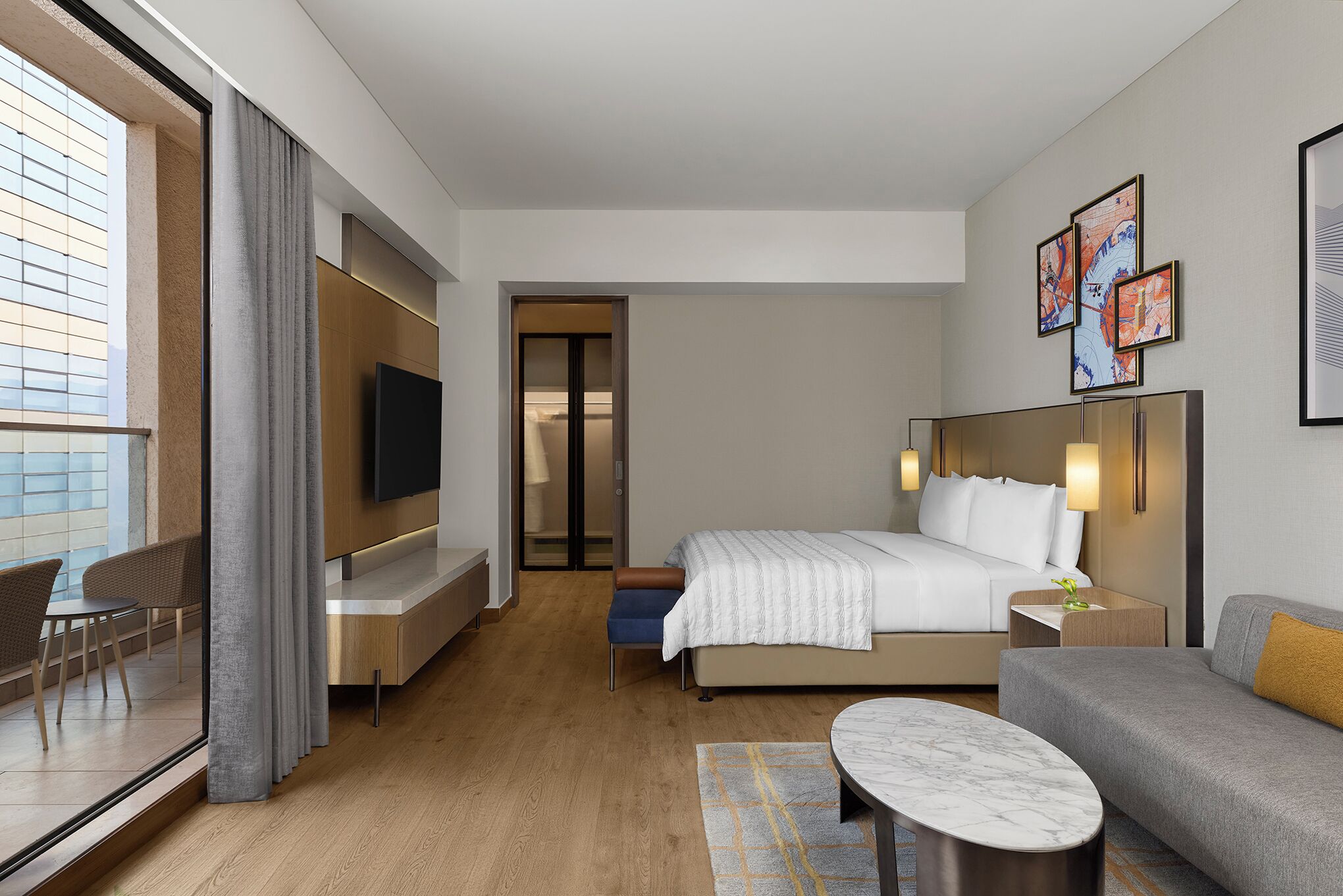 A modern hotel room with a bed, a TV, a seating area, and artwork on the walls.