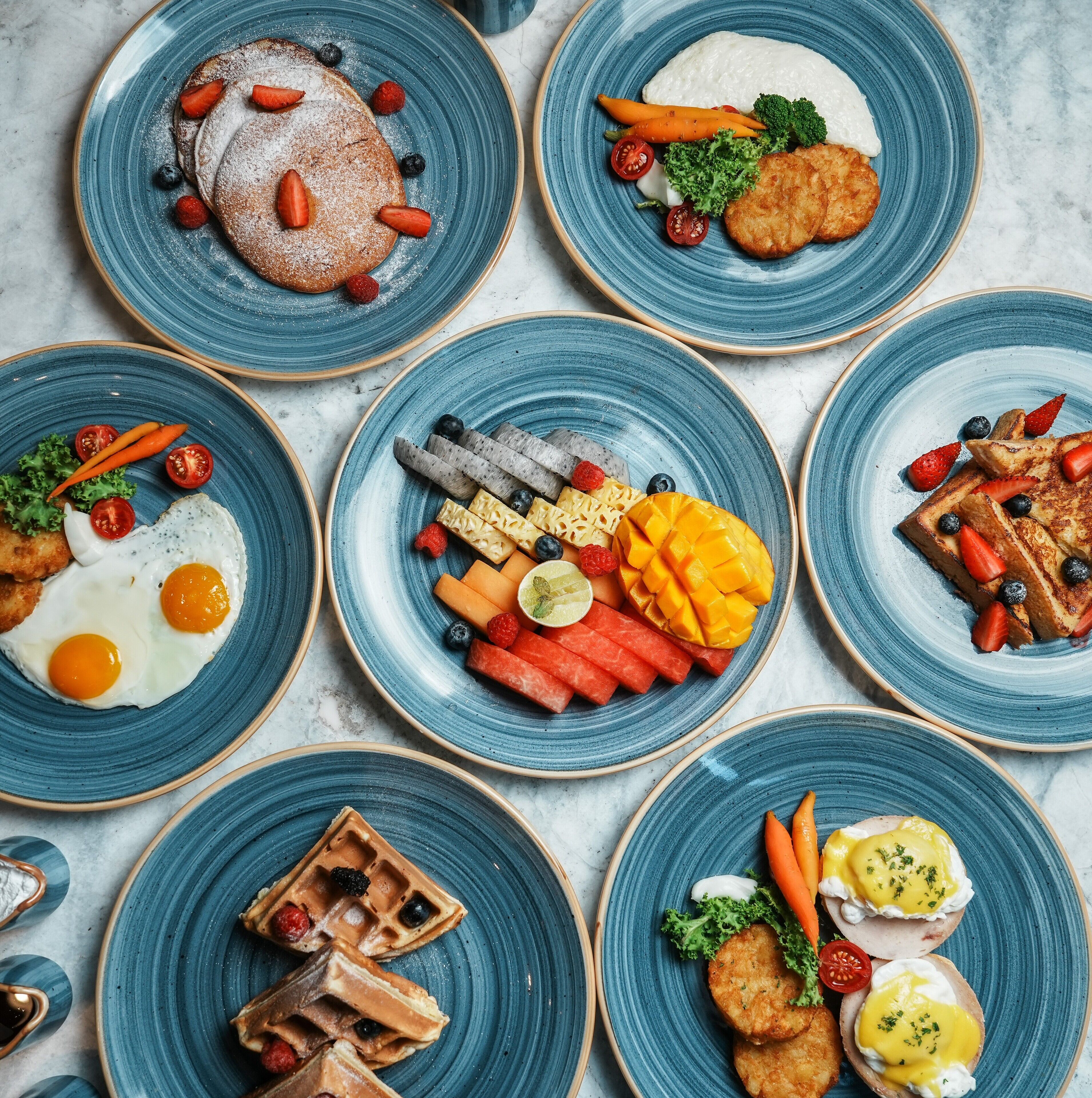 A variety of breakfast dishes on blue plates, including pancakes, eggs, waffles, and fruit.