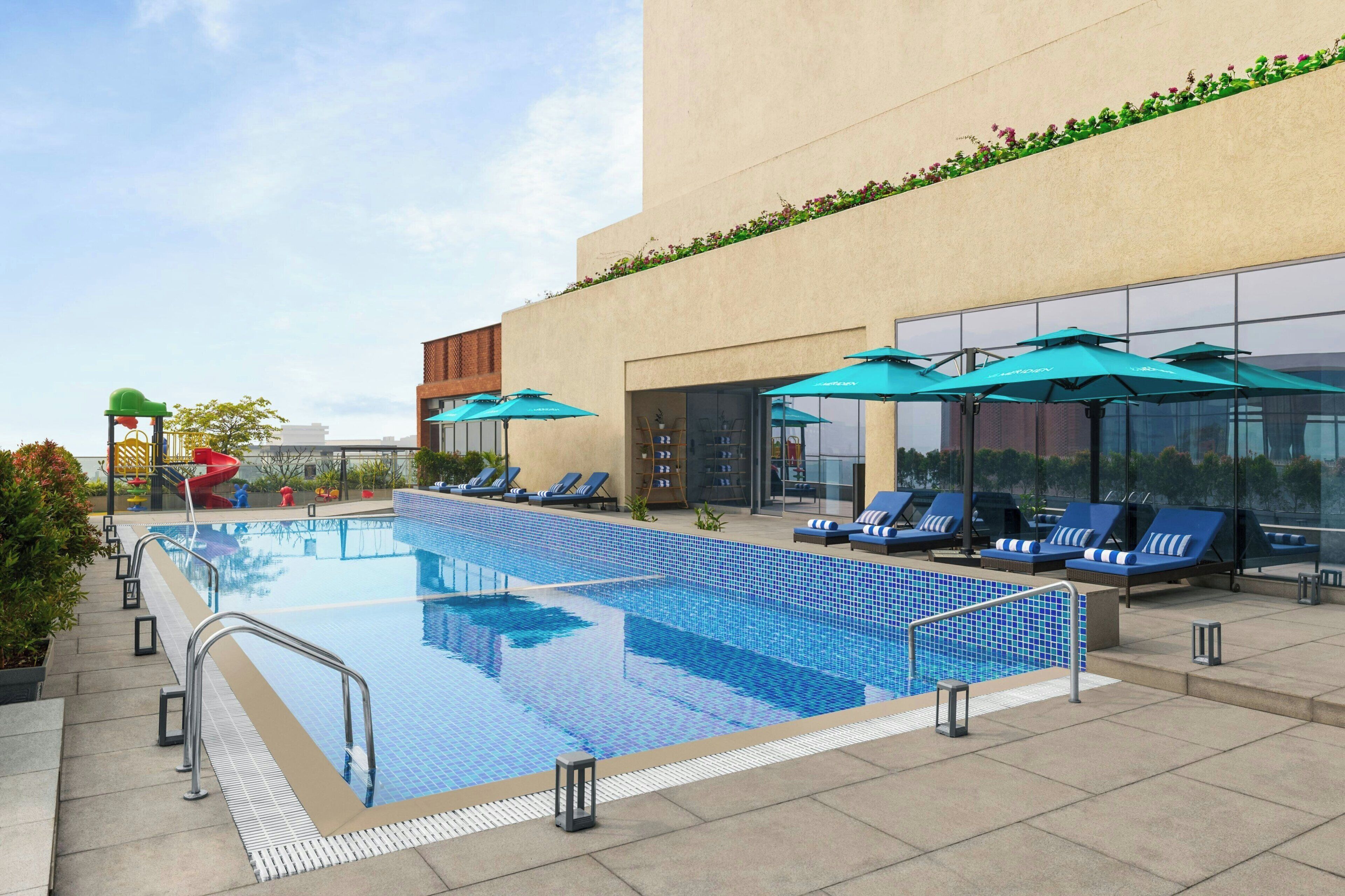 A rooftop pool with blue-tiled water, sun loungers, and umbrellas.