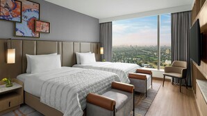 Een moderne hotelkamer met twee bedden, een groot raam met uitzicht op de stad, een flatscreen televisie en een zithoek.