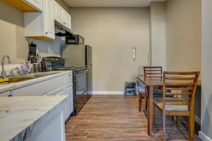 A compact kitchen with white cabinets, a microwave, stove, and a dining table with chairs.