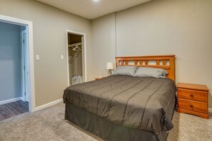 A bedroom with a large bed, a wooden nightstand, a bedside table, and a closet with a hanging rack.