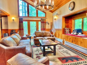 A cozy living room with leather sofas, a wooden coffee table, and a large window with a view of trees.