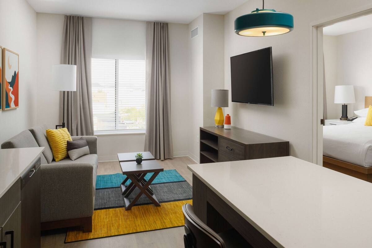 A modern hotel room with a sofa, a dining table, a TV, and a bed.