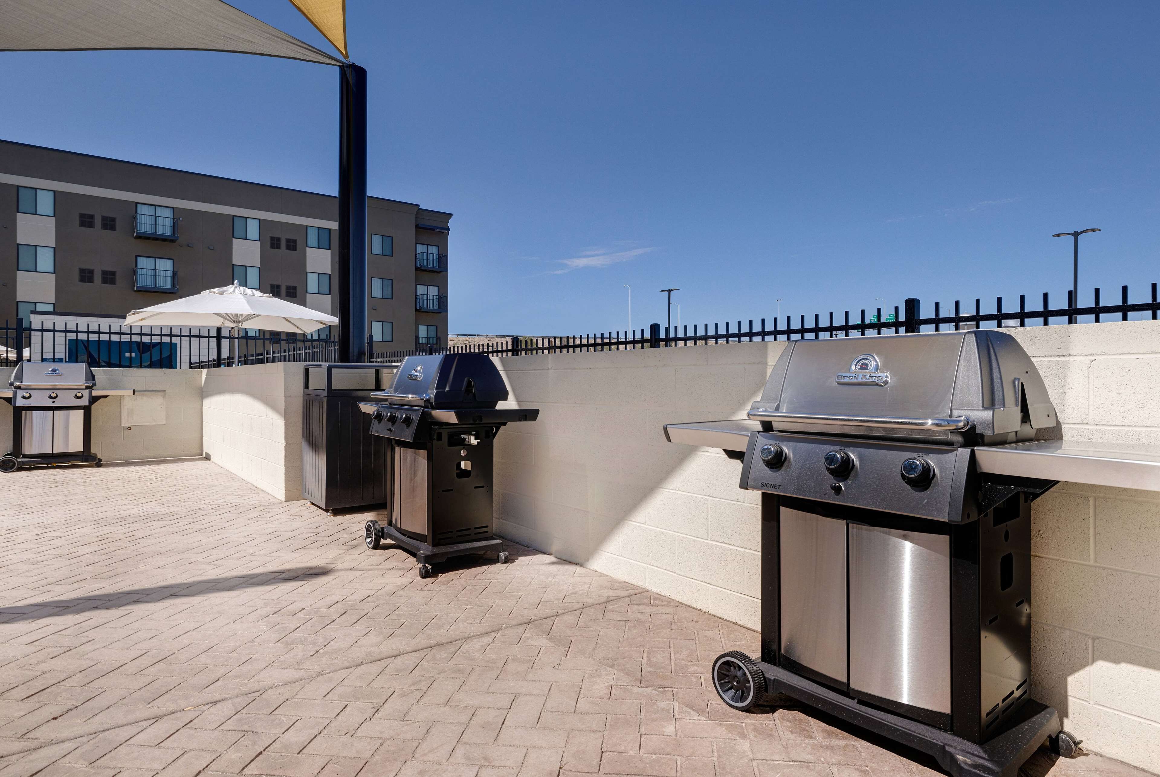 Un patio al aire libre con dos parrillas de barbacoa, un paraguas blanco y piso de ladrillo.