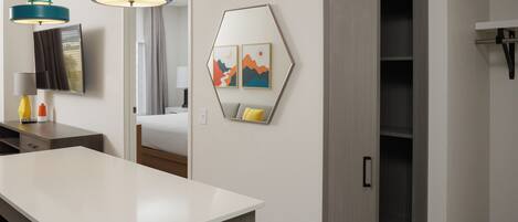 A modern hotel room with a large white desk, two teal pendant lights, a bed with a view, a wardrobe, and a wall-mounted TV.