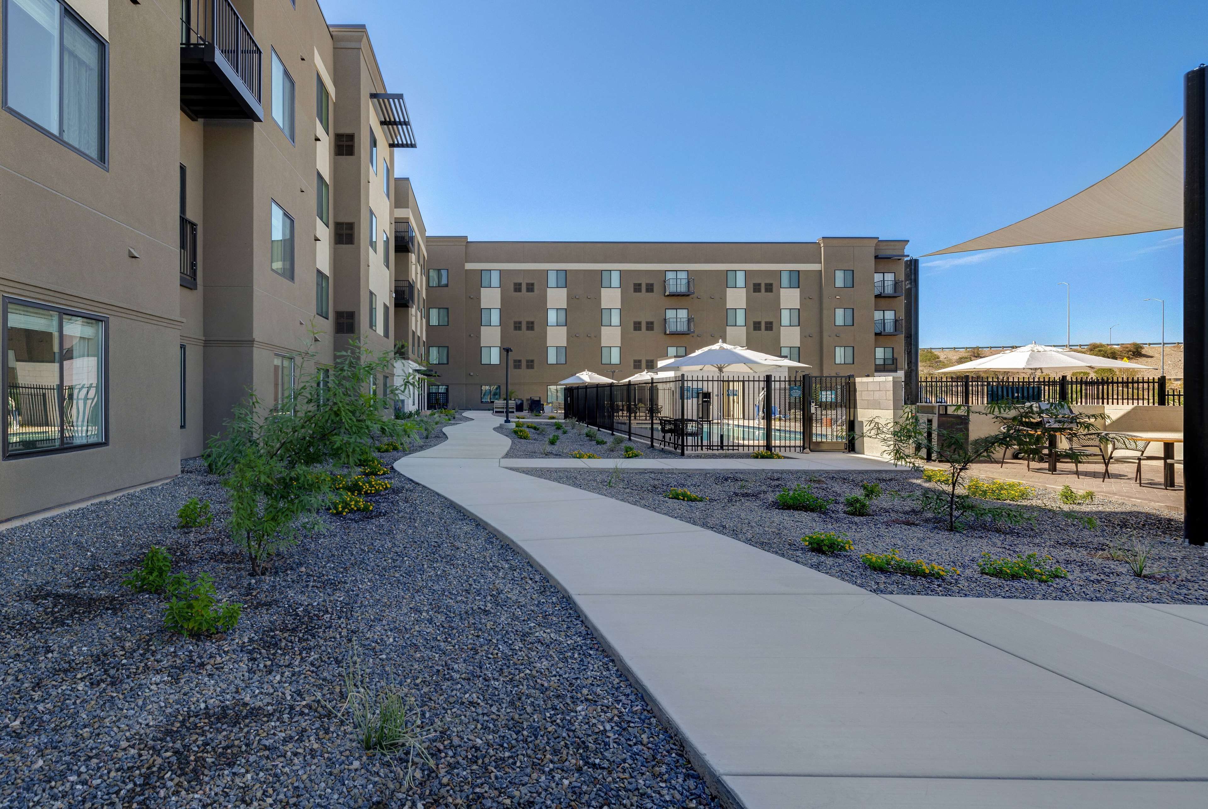A modern apartment building with a central courtyard featuring a pathway, outdoor seating, and a pool area.