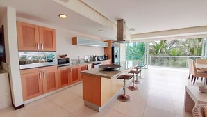 A modern kitchen with a central island, stainless steel appliances, and a large window overlooking a tropical landscape.
