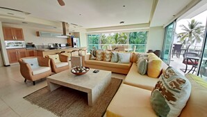 A modern living room with a sofa set, a coffee table, and a kitchen area visible through an open door.