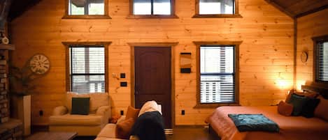 A log cabin with a loft bedroom, a living room with a sofa and armchair, and a dining area with a table and chairs.