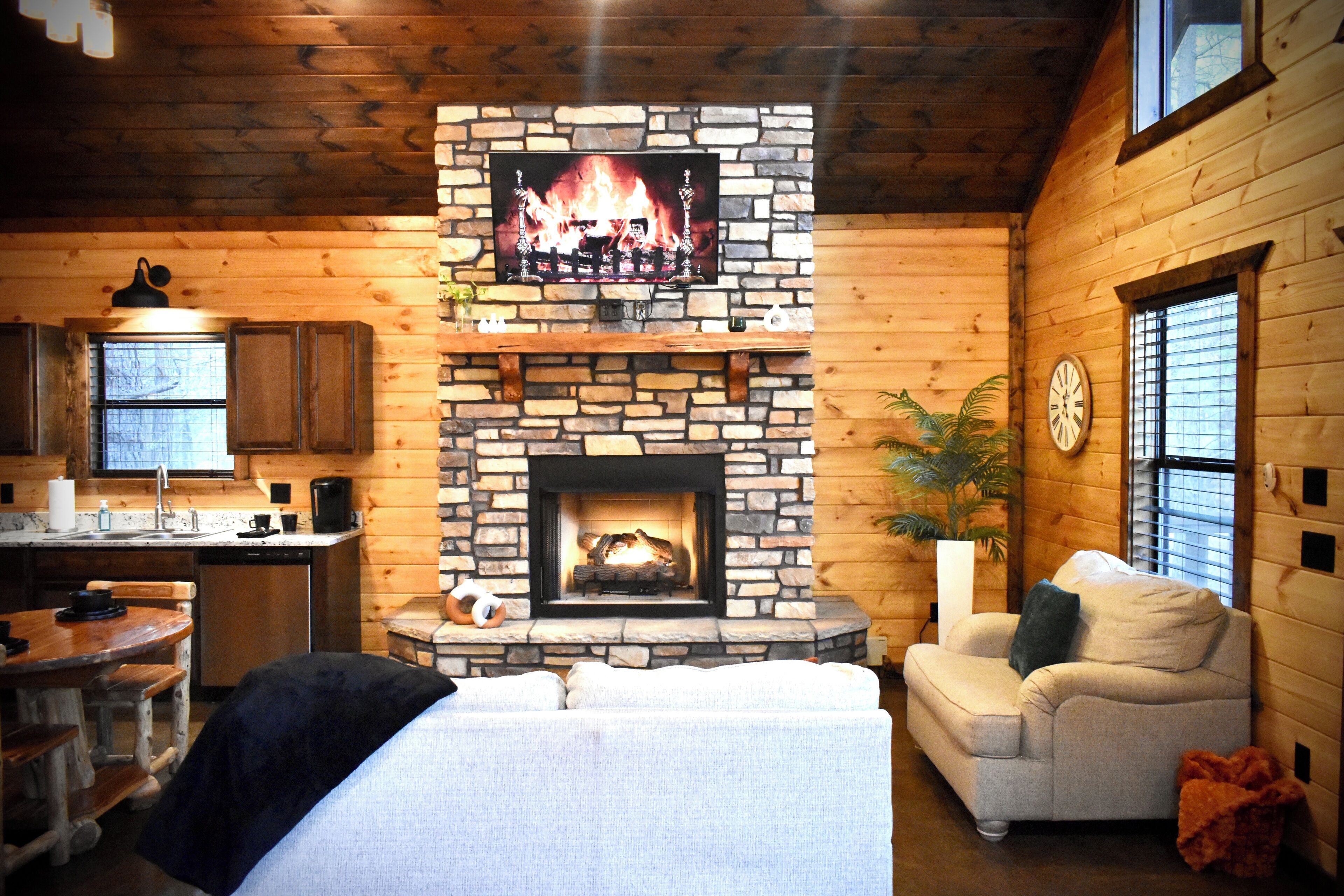 A cozy cabin interior with a stone fireplace, wooden walls, a dining area, and a living room with a sofa.