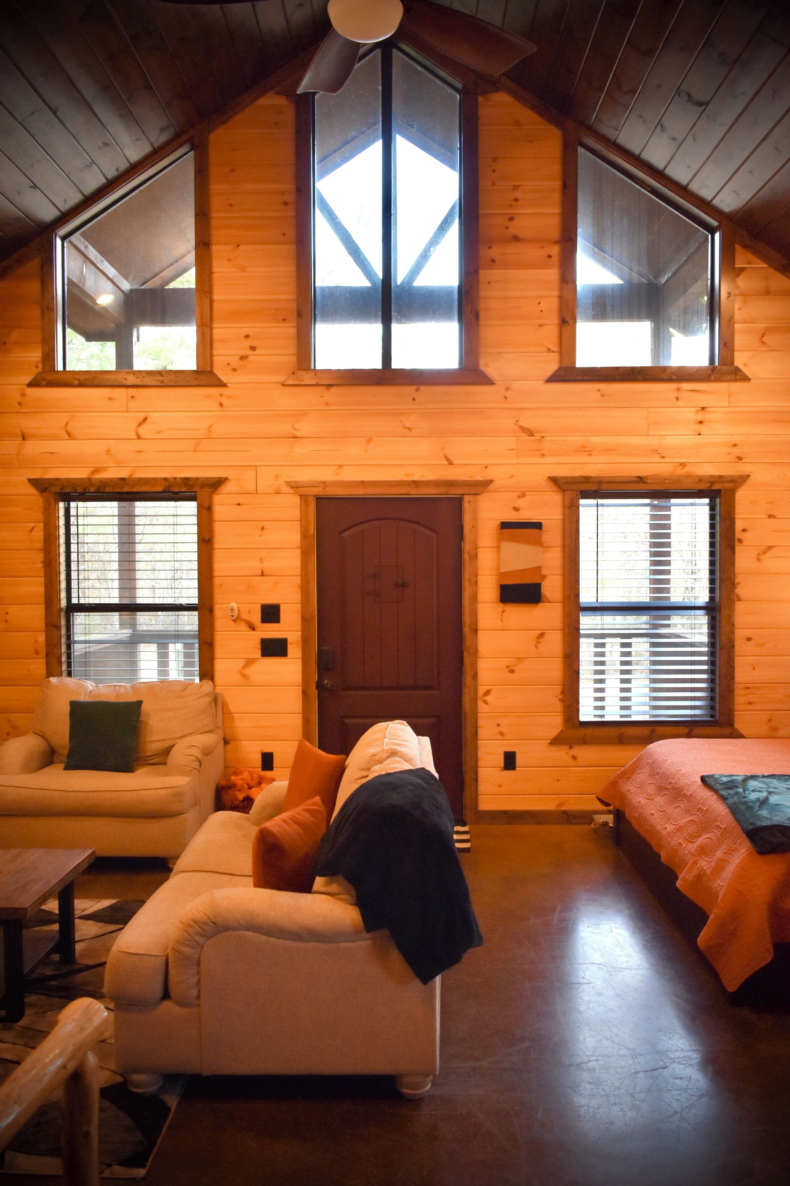 L’intérieur d’une cabane en rondins comprend une chambre à coucher située en mezzanine, un espace de vie avec un canapé et un fauteuil, et un plafond en bois.