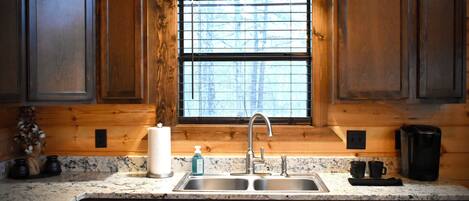Una cocina con armarios de madera, un lavamanos doble y una ventana con persianas.