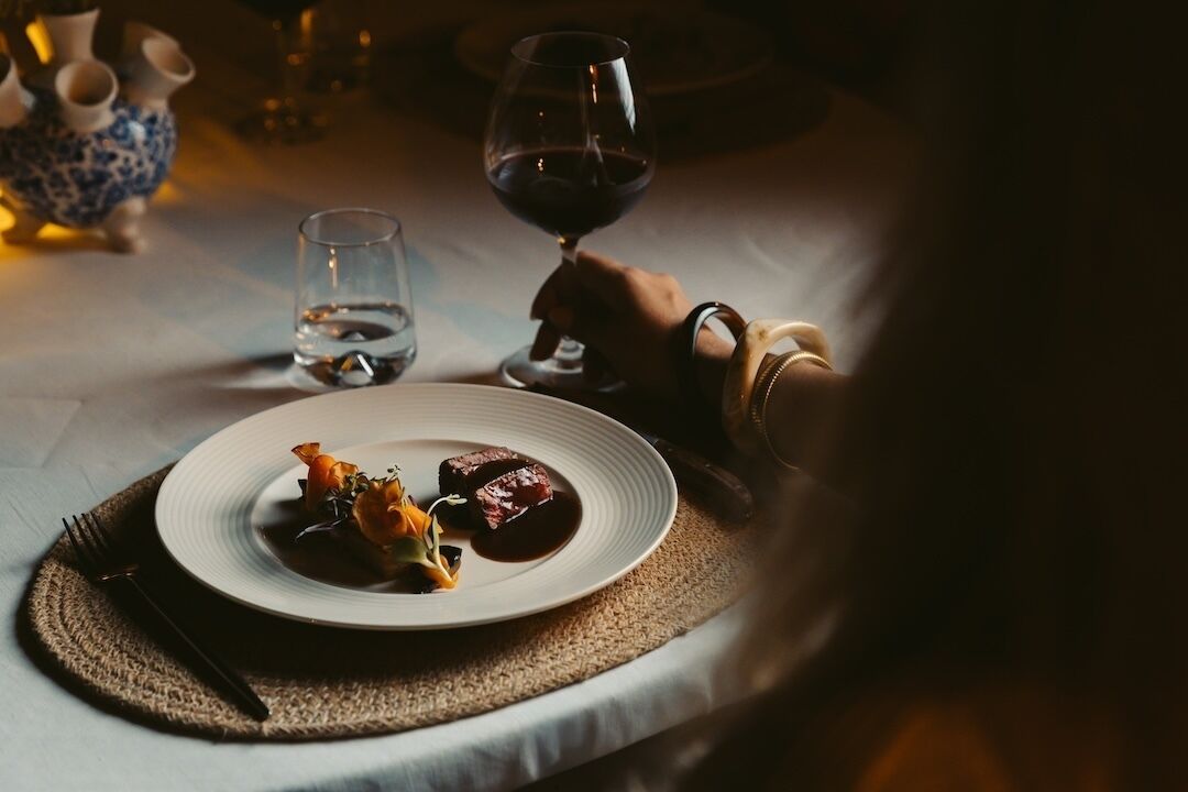 A dining table with a plate of food, a glass of red wine, and a water glass.