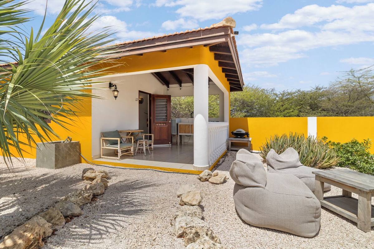 Un edificio amarillo con un porche cubierto, mesas al aire libre y vistas del paisaje circundante.