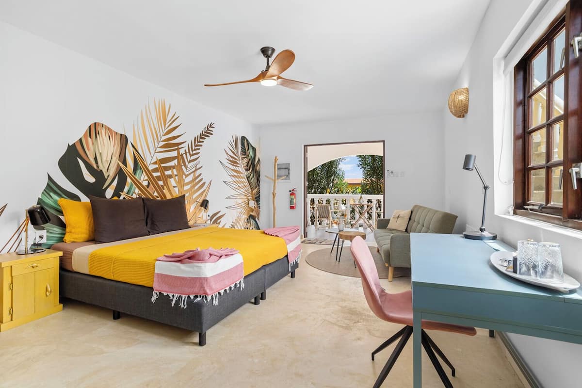 Un dormitorio moderno con cama, escritorio y silla, ventilador de techo y vistas al exterior.