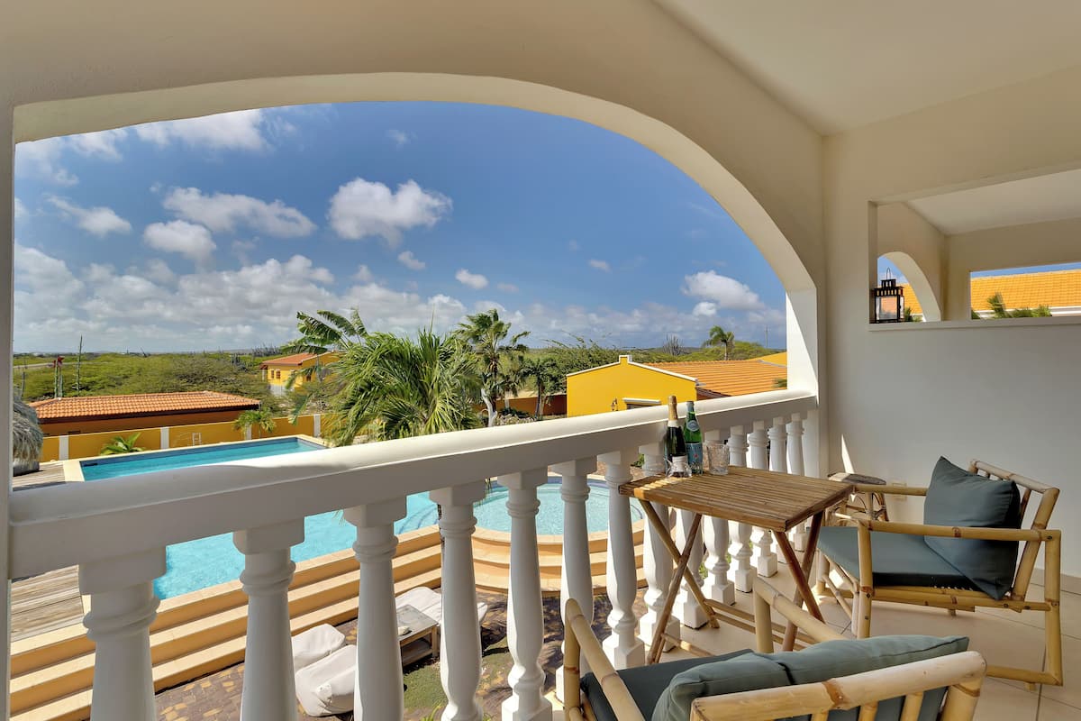 Un balcón con vista a una piscina, mobiliario exterior y cielo despejado.
