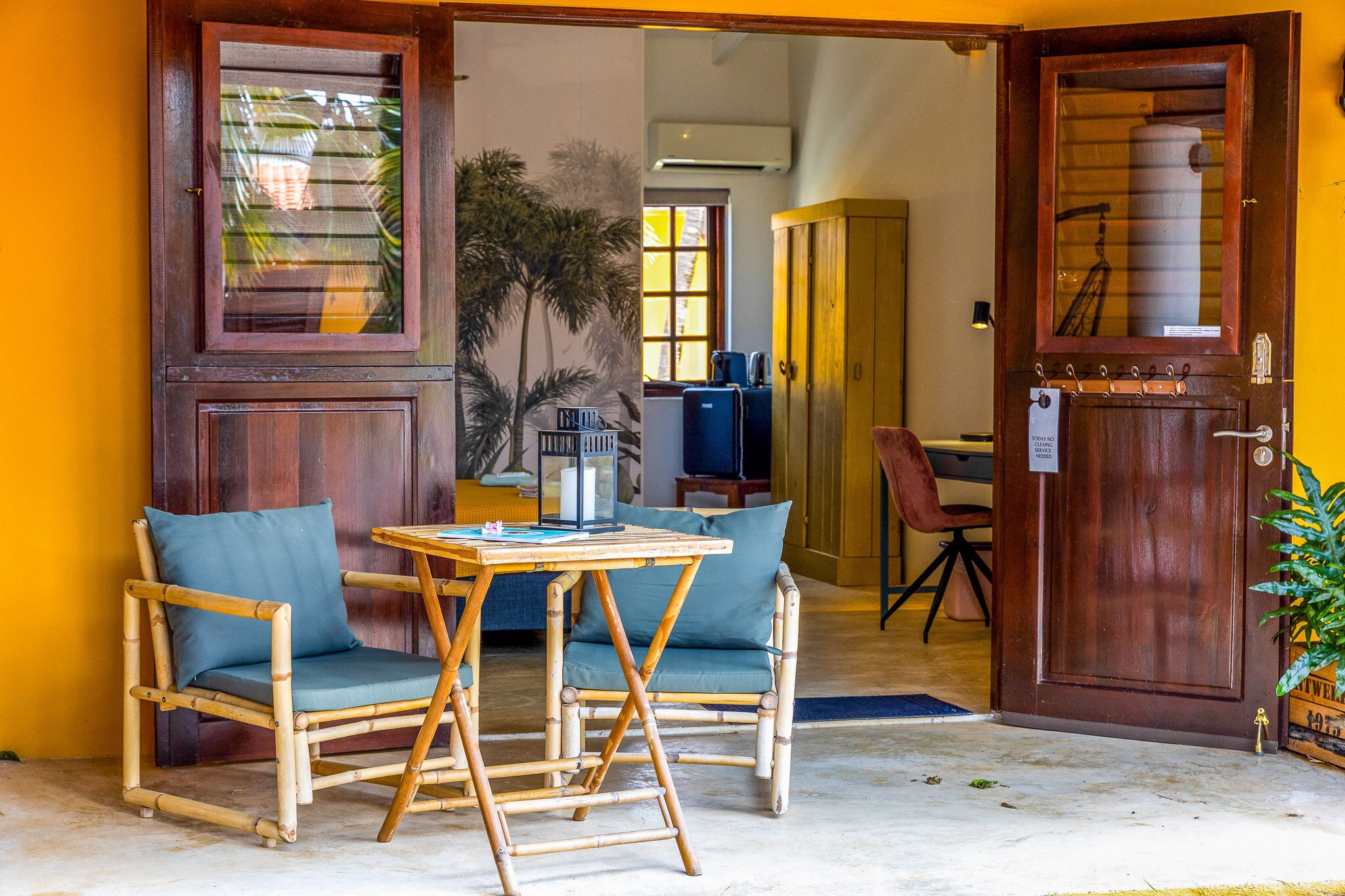 Una habitación con puerta de madera, una mesa pequeña con sillas y vistas al exterior.