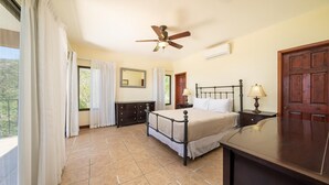A bedroom with a bed, bedside tables, a ceiling fan, a mirror, and a view of the outdoors. - Oceanview Condo With Pool Near Playa Prieta 2BR - Vida de la Paz 4 (Tempate)