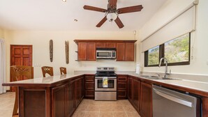 A kitchen with wooden cabinets, a built-in microwave, an oven, a dishwasher, and a large window providing a view of the outdoors. - Oceanview Condo With Pool Near Playa Prieta 2BR - Vida de la Paz 4 (Tempate)