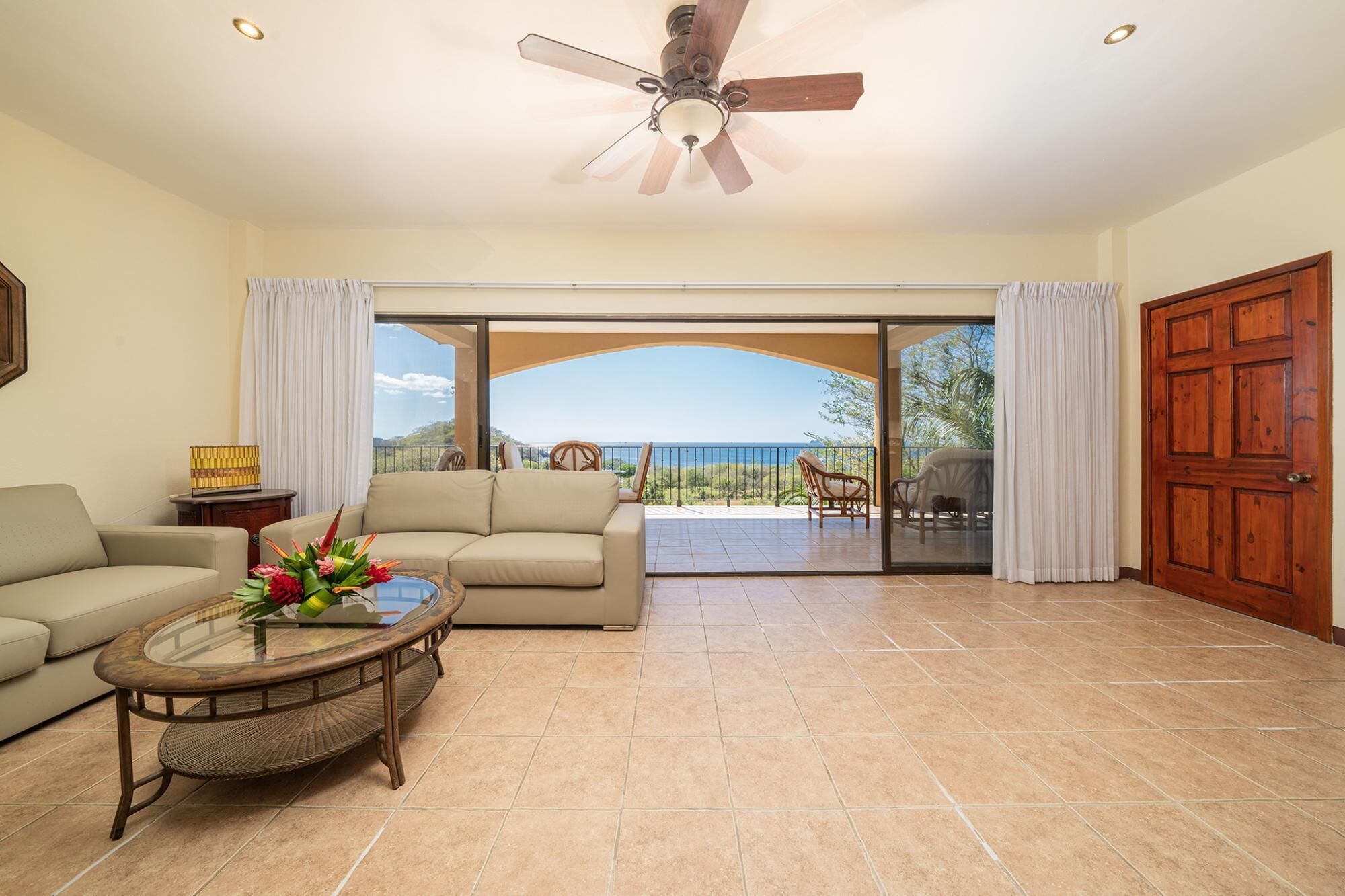 A spacious living room with a large sliding glass door leading to a balcony with a view of the ocean.