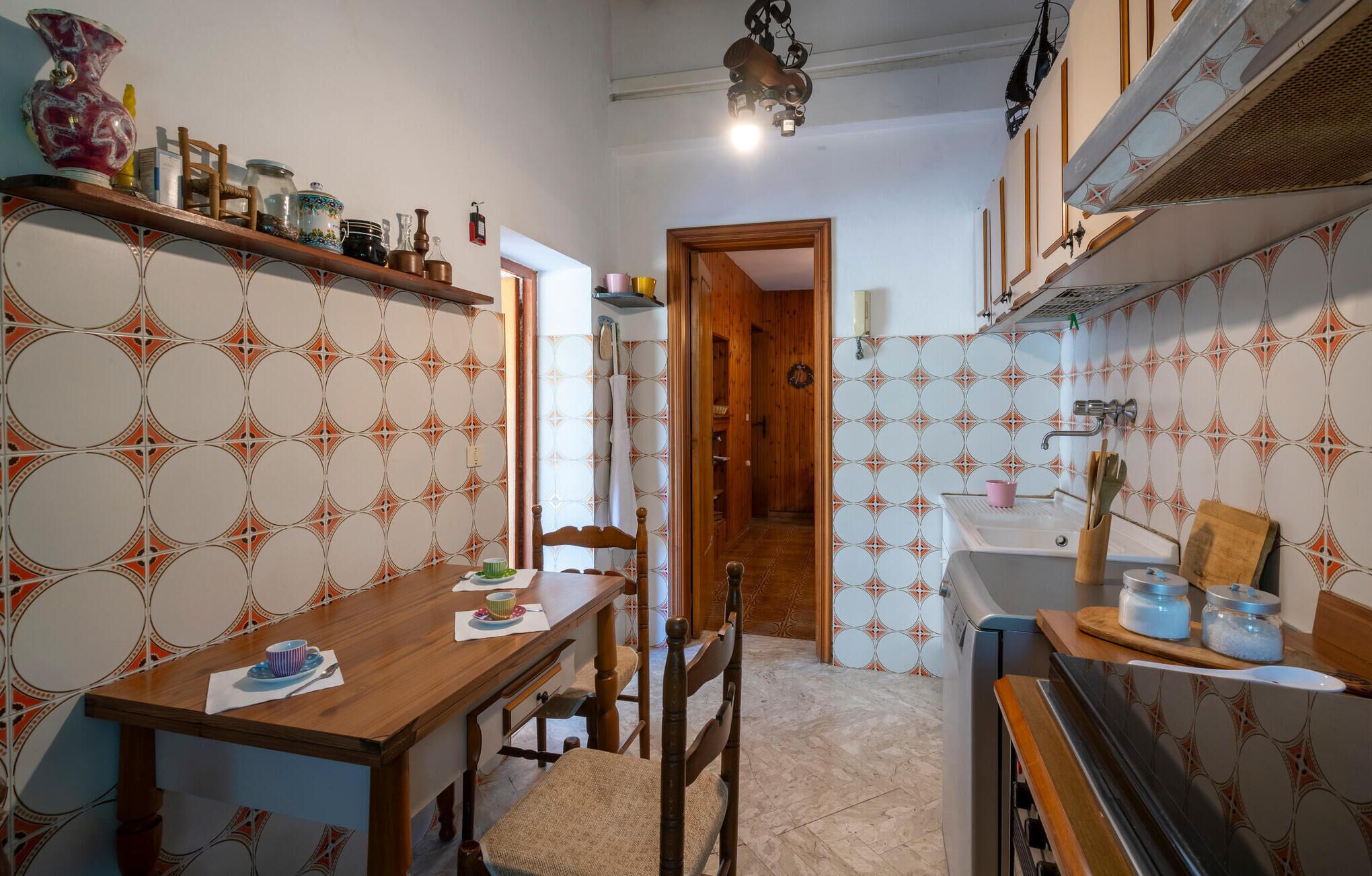 Une cuisine de taille réduite, avec une table et des chaises en bois, un luminaire suspendu et un papier peint à motifs.