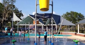 Enjoy water play and fun in the sun under a shaded area with a large water tower and water jets.