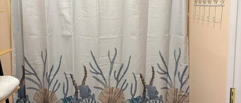 A bathroom with a shower curtain featuring a marine design, a toilet, a small trash bin, and a wall-mounted hook rack.