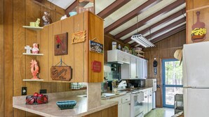Une cuisine rustique avec des murs en bois, un îlot central en bois avec des tabourets, un four à micro-ondes, une cuisinière et divers ustensiles de cuisine.
