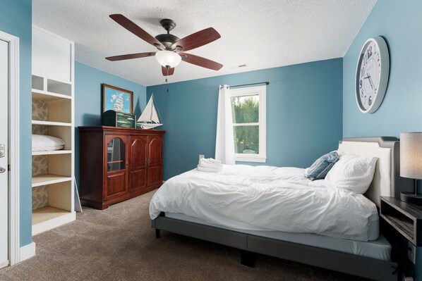 Quarto com cama, ventoinha no teto, relógio, janela e guarda-roupa.